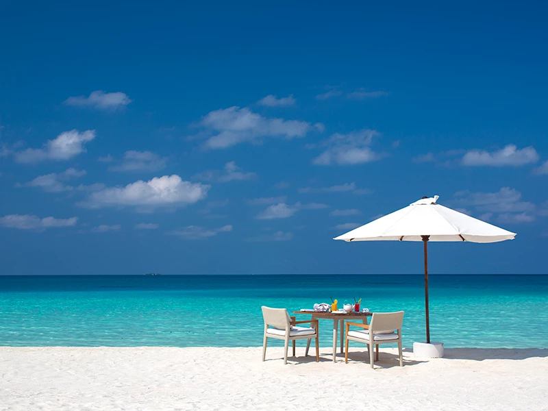 Strand med en hvid parasol, et bord og to stole